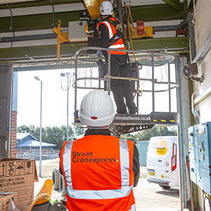 two street cranexpress engineers working on a crane, one is on the ground and the other is on a platform