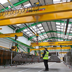 A person using a crane in a factory lifting a metal structure