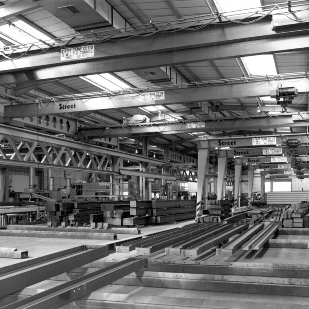 A large factory full of cranes with metal beams on the floor