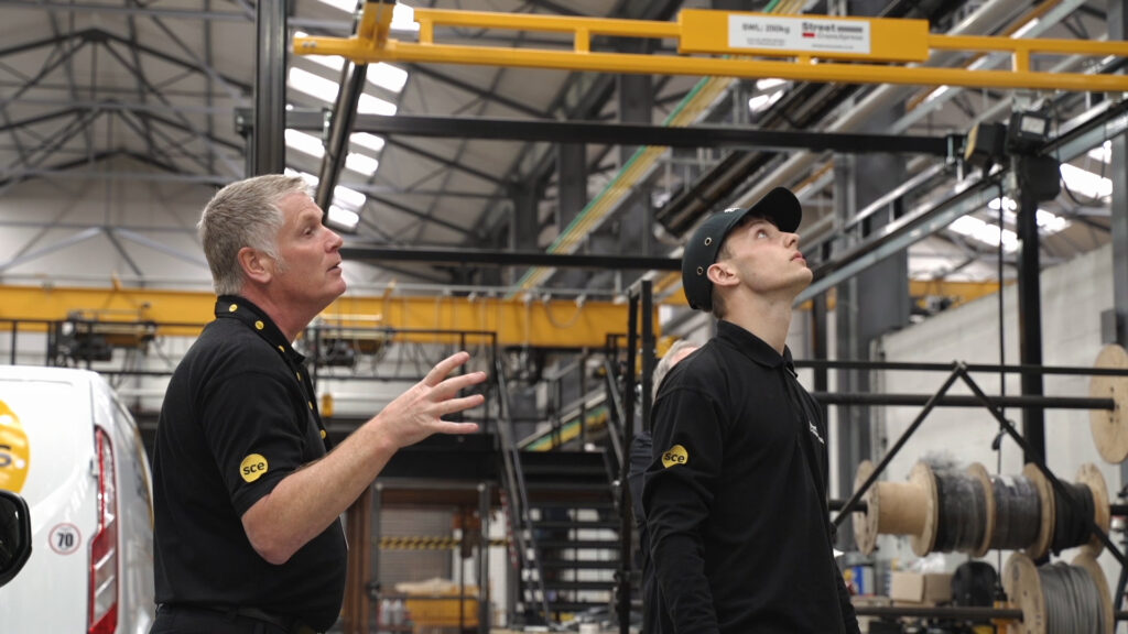 Two men in a warehouse examining a light crane system