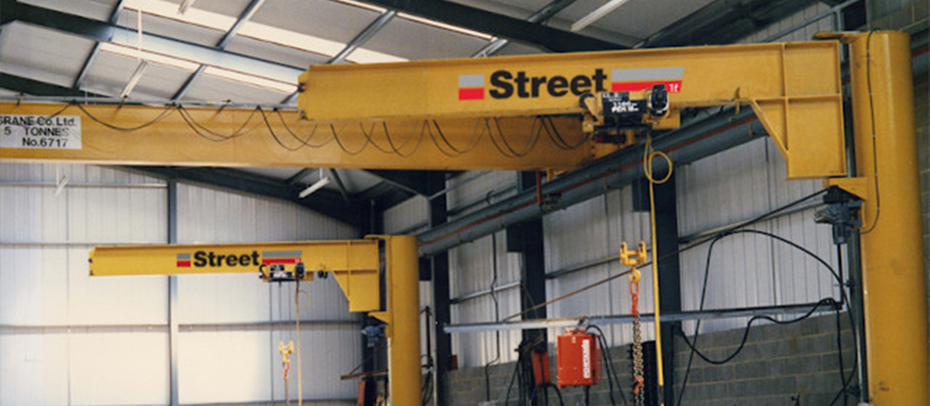 two post mounted yellow jib cranes and a single girder crane in a warehouse